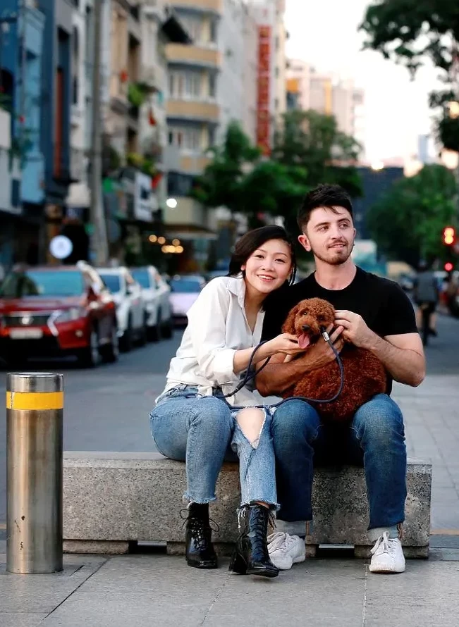 Young couple with dog sitting on stone bench in the city